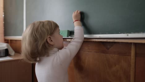 girl drawing at blackboard using a chalk in classroom. education process