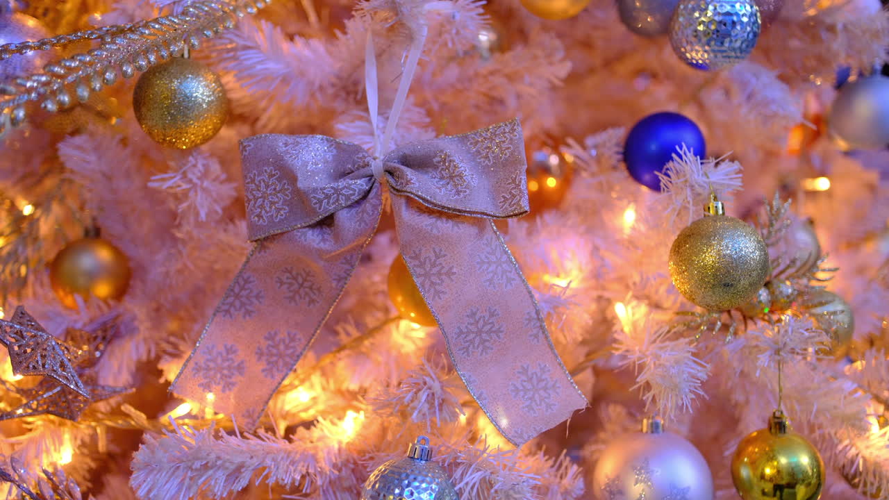 White christmas tree decorations with flashing lights. Elegant white christmas tree with bow, balls, and ornaments illuminated by festive changing lights