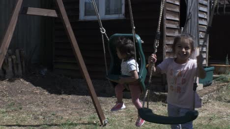 cute baby and older sister together on swing set in the garden