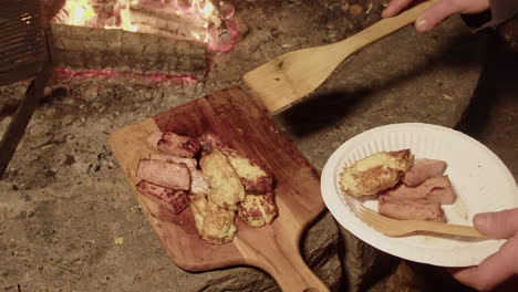 Tasty-fried-ham-and-cheese-slices-by-fire-pit-put-onto-paper-plate