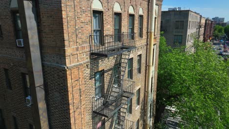 Aerial-descending-shot-of-old-apartment-complex-in-New-York-City-with-fire-escape-and-window-air-conditioning-units-in-summer