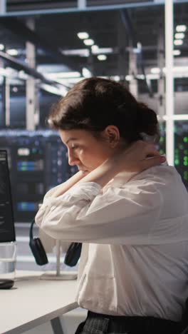 Vertical video Fatigued data center engineer stretching, monitoring server clusters
