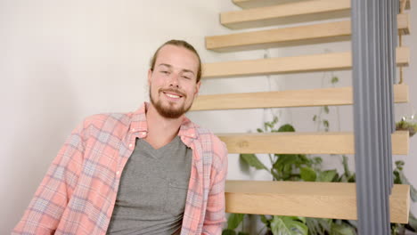 A-young-biracial-man-smiles-warmly,-seated-indoors-at-home