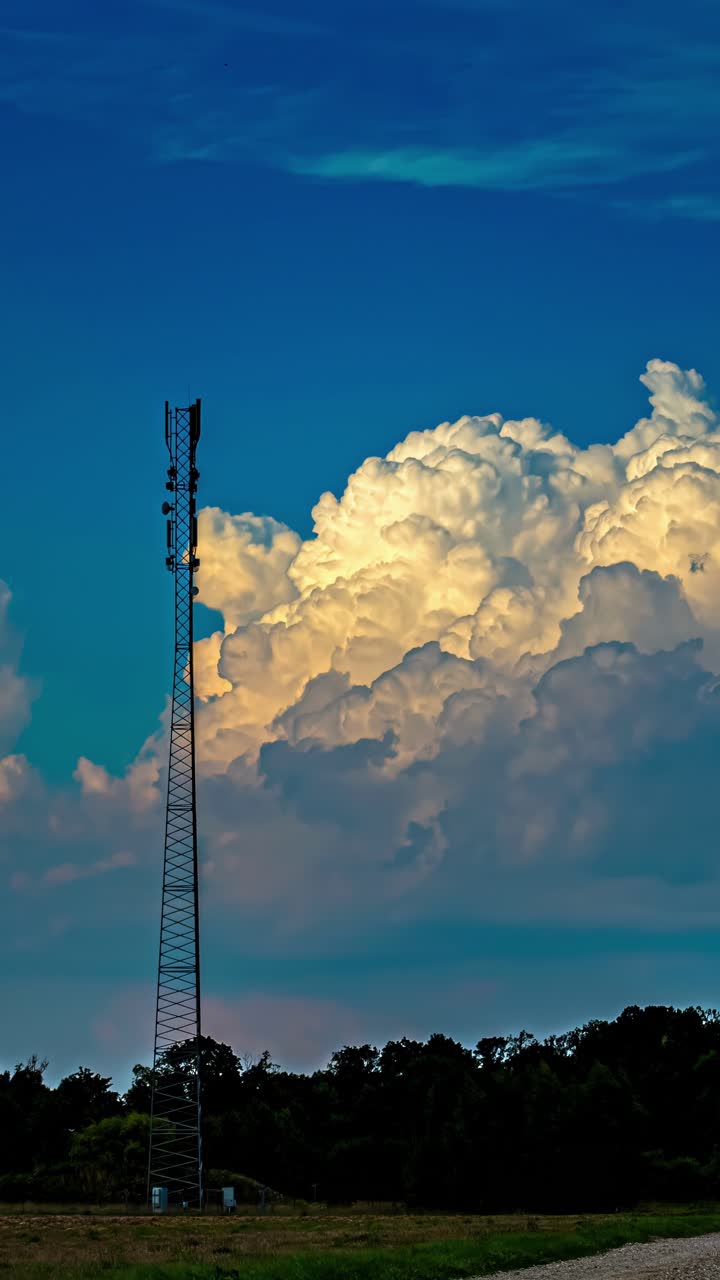 Timelapse of fluffy white clouds drifting across bright blue sky horizon growing and dissapearing behind telecommunications tower, vertical