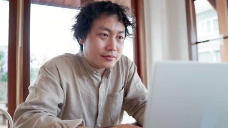 asian man looking at silver laptop computer in the cafe during daytime