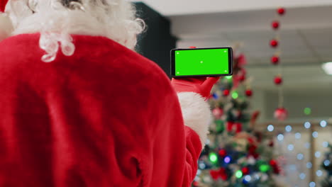 Employee-in-festive-ornate-shopping-mall-wearing-Santa-Claus-suit-holding-green-screen-phone,-taking-a-break-from-job-shift-and-watching-videos-on-chroma-key-screen,-close-up