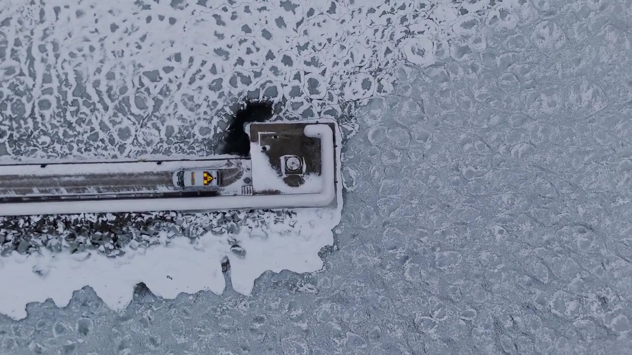 En imponerende dronevideo fanger et fugleperspektiv av en snødekt brygge og et parkert kjøretøy som strekker seg ut i det frosne vannet i Vättern i Jönköping, Sverige