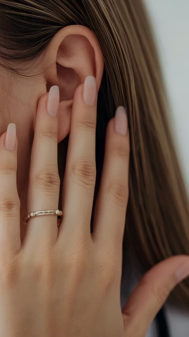 Vertical video: Recording woman smoothing hair behind left ear in studio, showing ring and manicure