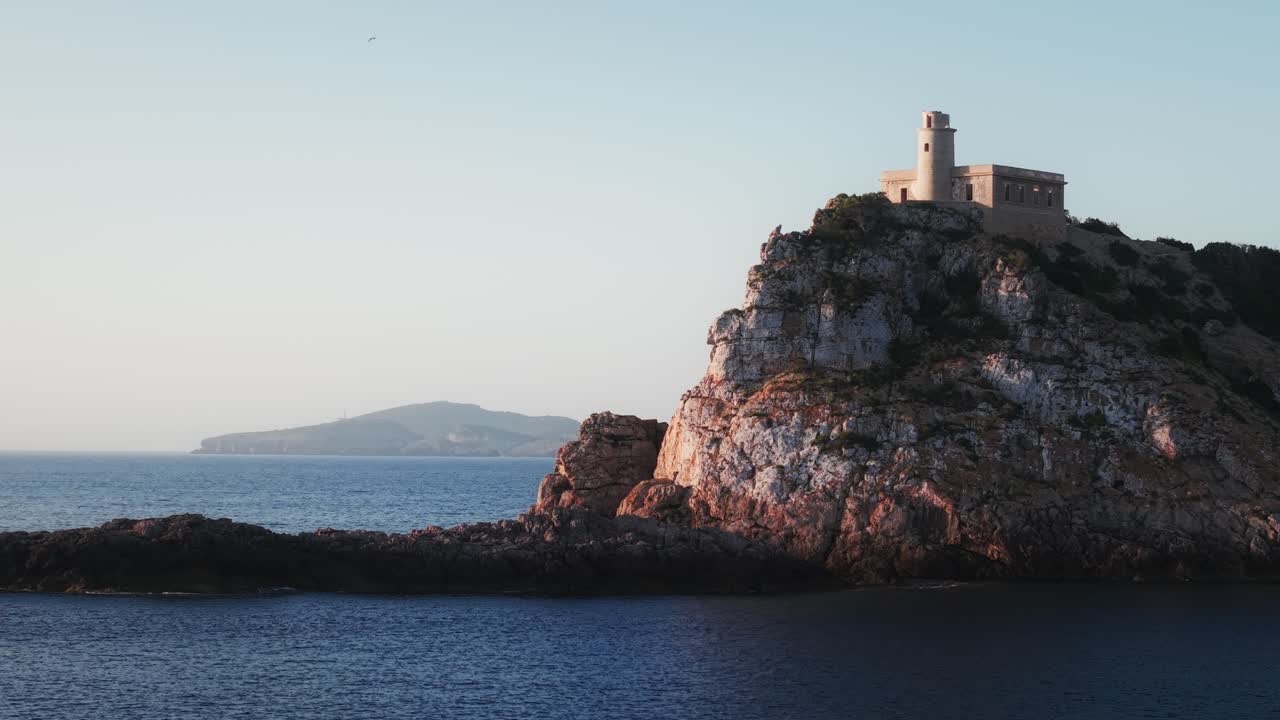 Orbita di drone intorno al Faro di Punta Grossa che rivela l'isola di Tagomago nella luce dorata di Ibiza.