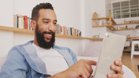 hombre alegre usando una tableta digital mientras está sentado en una bolsa de frijoles en el interior