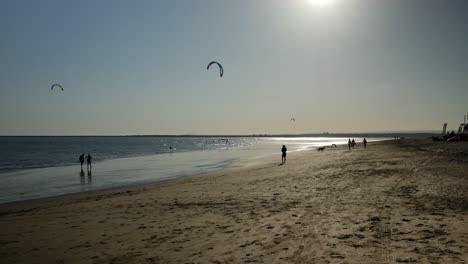 two kitesurfers and some people at sunset on the beach