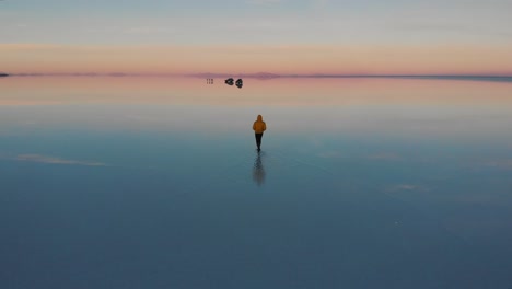 Un-Joven-Con-Una-Chaqueta-Amarilla-Caminando-Sobre-Un-Salar-Inundado-En-Bolivia-Durante-El-Amanecer