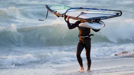 Male-surfer-carrying-windsurfer-in-the-beach-4k