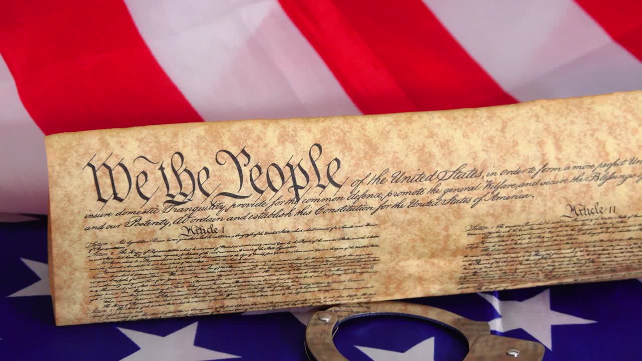 Symbolic image of handcuffs restraining the US Constitution against the backdrop of the USA flag representing the tension between freedom rights justice and the rule of American law