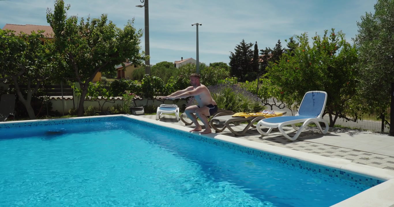 Mand træner alene ved en swimmingpool, mens han udfører kropsbøjninger. Udendørs fitness, udstrækning, mobilitetstræning og sund livsstil på en solrig dag.