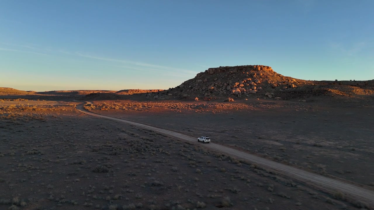Veduta aerea di un SUV bianco su una strada nel deserto in un paesaggio arido dello Utah, USA, ripresa con drone.