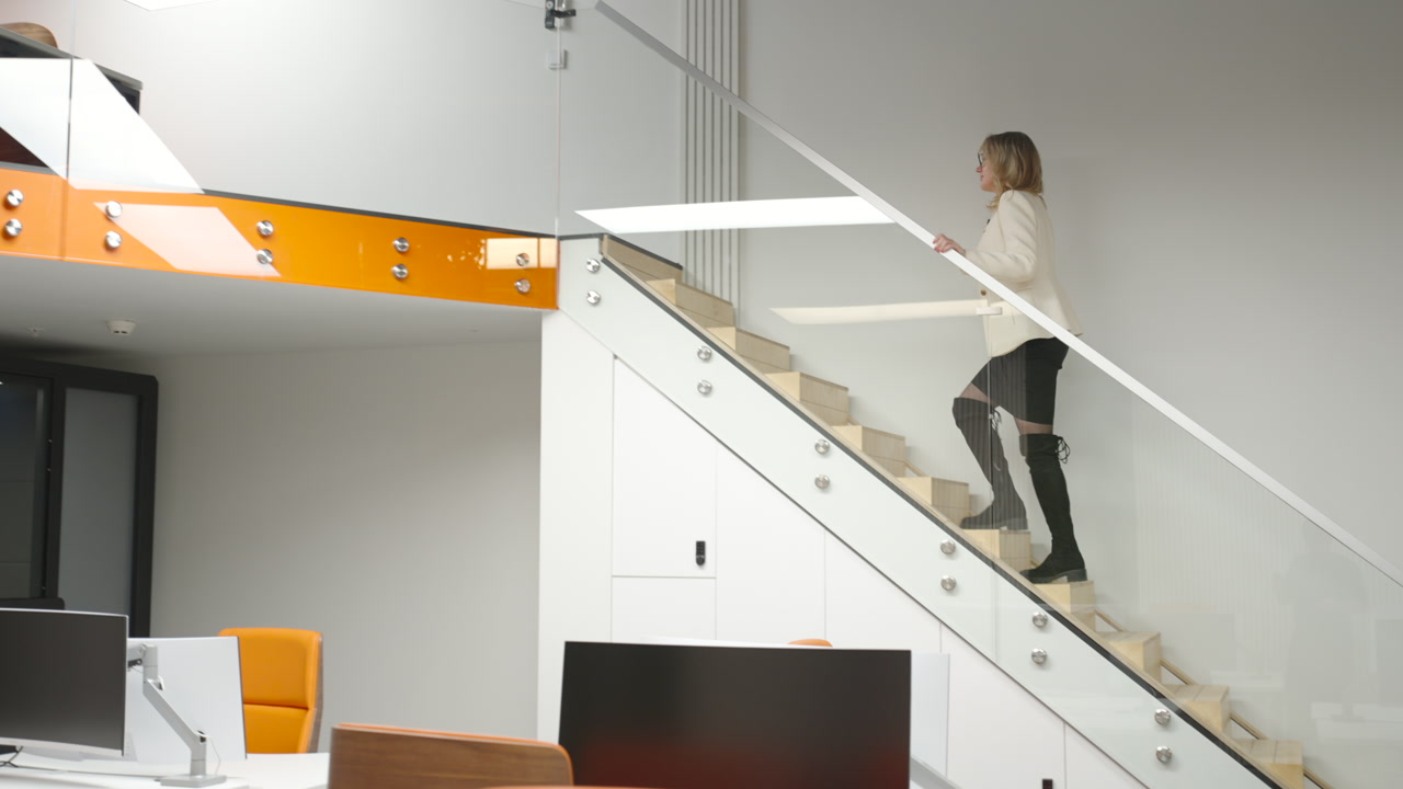 Female Employee Climbing Glass Staircase In Office Focused Stride Modern Open Plan Workspace Orange Accents. Creative