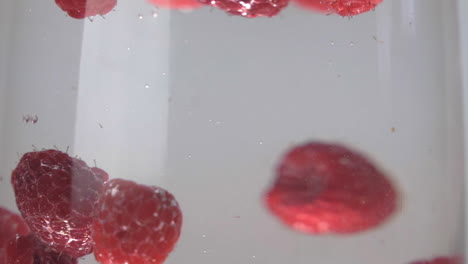 slow motion raspberries floating and splashing into glass of water up close