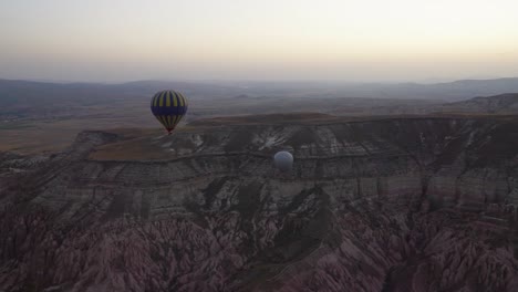 Vista-Aérea-De-Un-Globo-Azul-Y-Amarillo-Que-Vuela-Sobre-El-Valle-Rojo-De-Capadocia