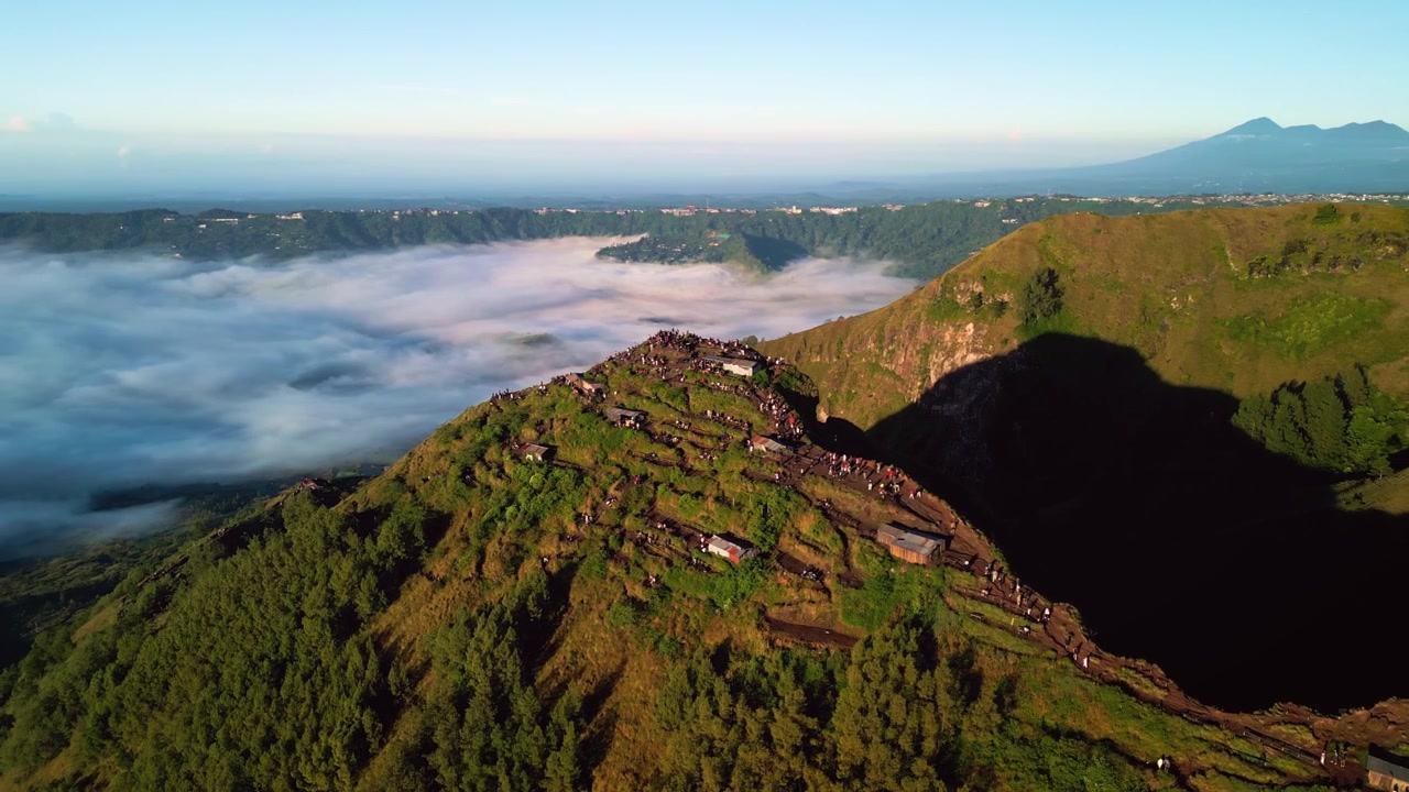 Mirante do nascer do sol no Monte Batur, caminhantes ao longo da crista da montanha observando o nascer do sol acima da camada de nuvens na luz da hora dourada, terreno vulcânico íngreme e paisagem da borda da cratera, filmagem aérea de drone.