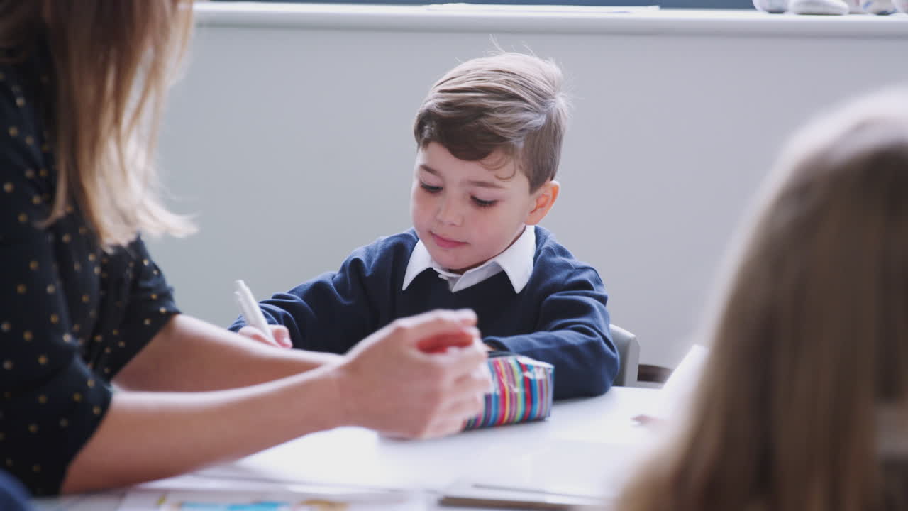 maestra sentada en una mesa con escolares en una lección de escuela primaria, enfoque selectivo