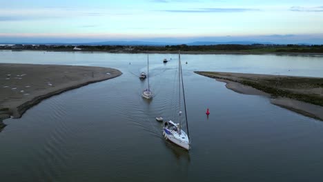 Yachts-being-followed-by-pilot-boats-into-marina-tributary-on-calm-water-at-dusk-on-the-River-Wyre-Estuary-Fleetwood-Lancashire-UK