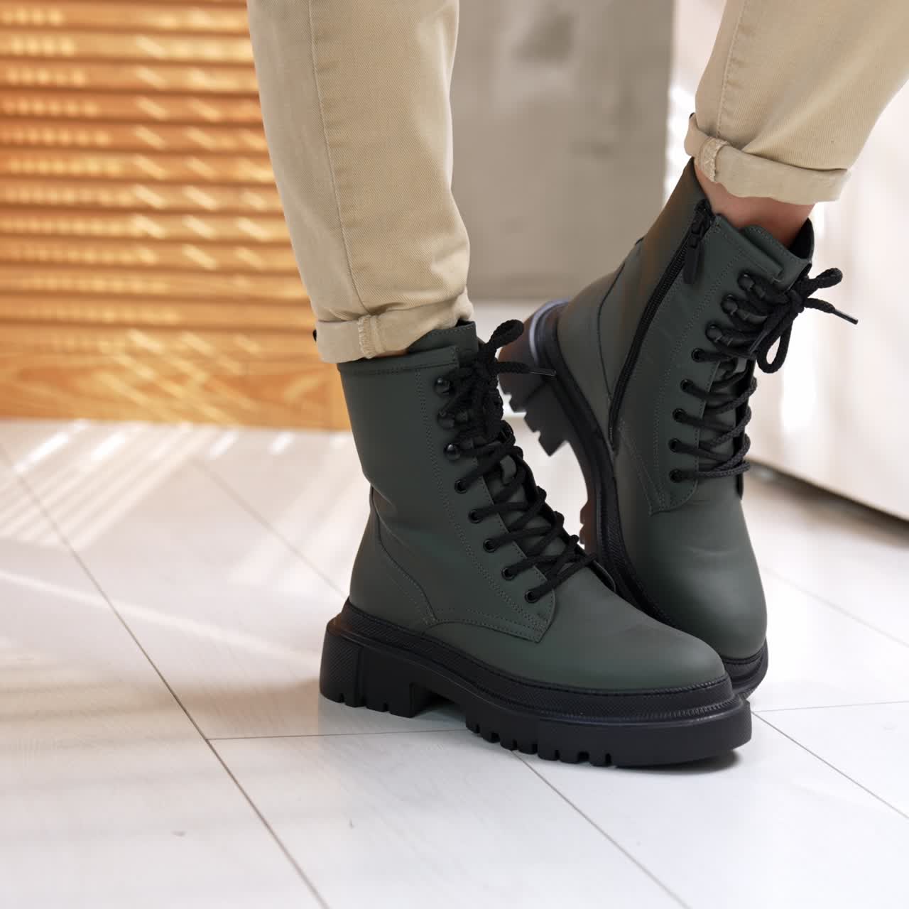 Grey elegant footwear with black laces and black tractor soles. Model in light jeans demonstrating stylish boots in studio