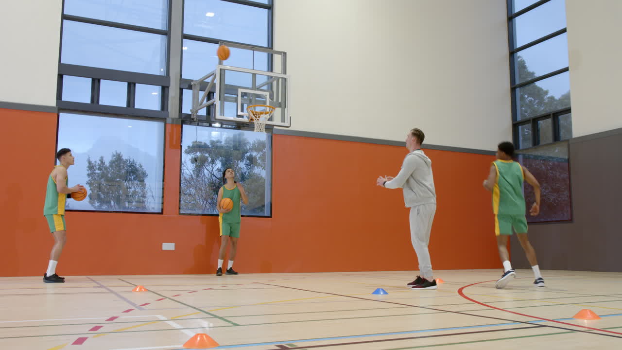 Multiracial male basketball players with coach in gym, running and throwing ball into basket