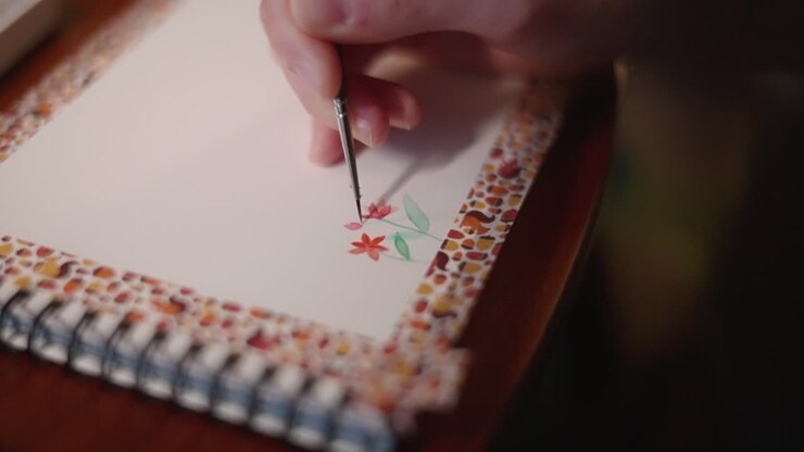 Painter Paints A Beautiful Red Flowers On Sketch Pad Using Watercolor And Paint Brush