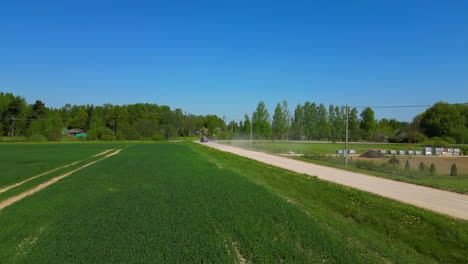 slow motion of two vehicles driving down a dusty country road next to a field on a clear and sunny summer day