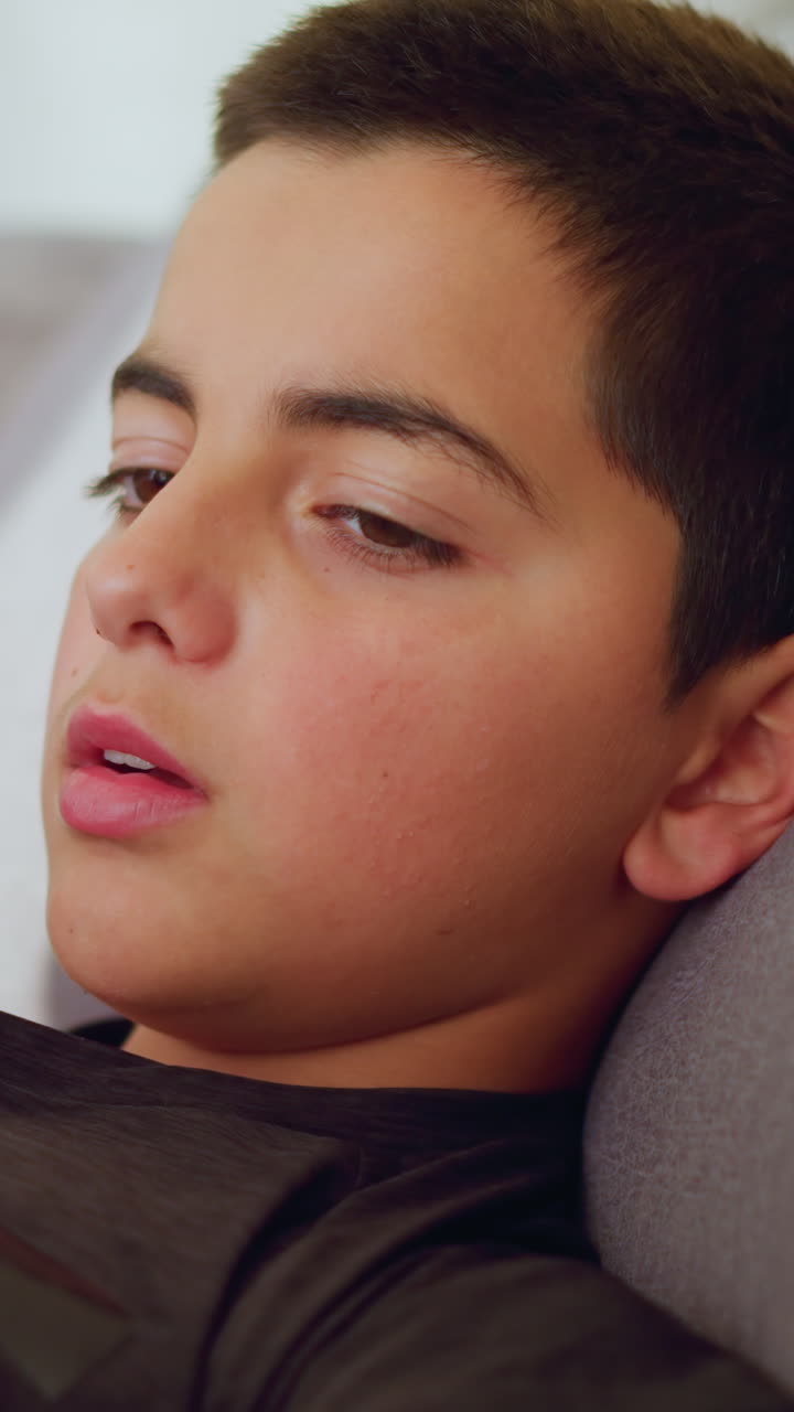 Close up of sick boy lying on couch under blanket looking at thermometer held by another person showing concern and awareness in calm indoor space