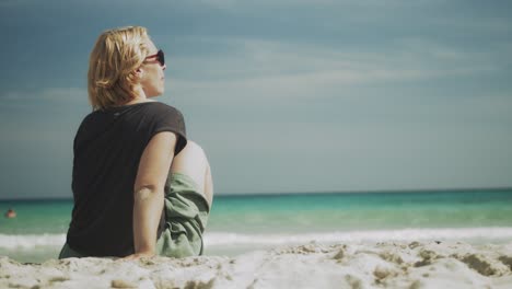 Woman-sitting-on-sandy-beach,-playing-with-the-sand,-relaxed-holiday-on-Mallorca