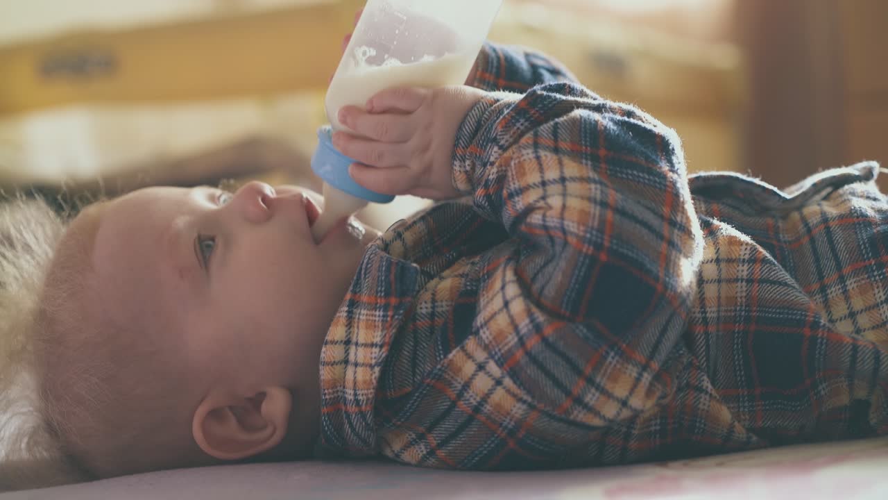 il piccolo bambino mangia un gustoso mix di latte da una piccola bottiglia sul letto