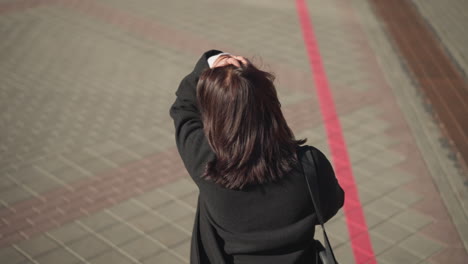 밖에서 고 머리를 만지고 손에 드폰을 들고 있는 여성이 활기찬 환경으로 도시 보행로를 따라 걸어가는 모습이 뒷면에서 명확하게 포착되어 있습니다.