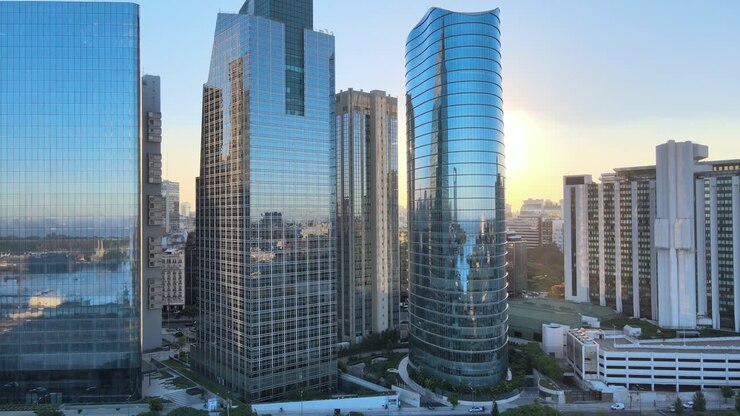 Establishing aerial pan shot of a beam of sunlight through the gap between shimmering reflective glass facade skyscrapers in downtown futuristic central business district of Buenos Aires at sunset