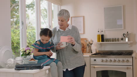 grandmother and little girl using smartphone watching online entertainment eating cookies in kitchen happy granddaughter enjoying sharing weekend with granny browsing internet on mobile phone