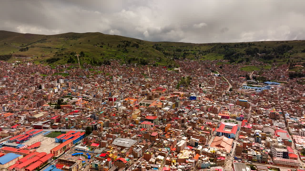 Pemandangan sinematik udara dari drone kota Puno yang luas, terletak di perbukitan hijau Andes. Ideal untuk konsep perjalanan Amerika Selatan dan pengembangan perkotaan, Peru