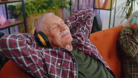 Felices-Abuelos-De-La-Familia-Senior-Hombre-Mujer-Con-Auriculares-Escuchando-Música-Relajándose-En-El-Sofá-En-Casa