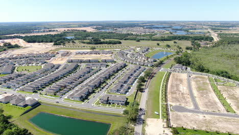 Flying-over-newly-constructed-neighborhood-surrounded-by-green-woods-and-rolling-fields-on-a-summer-afternoon