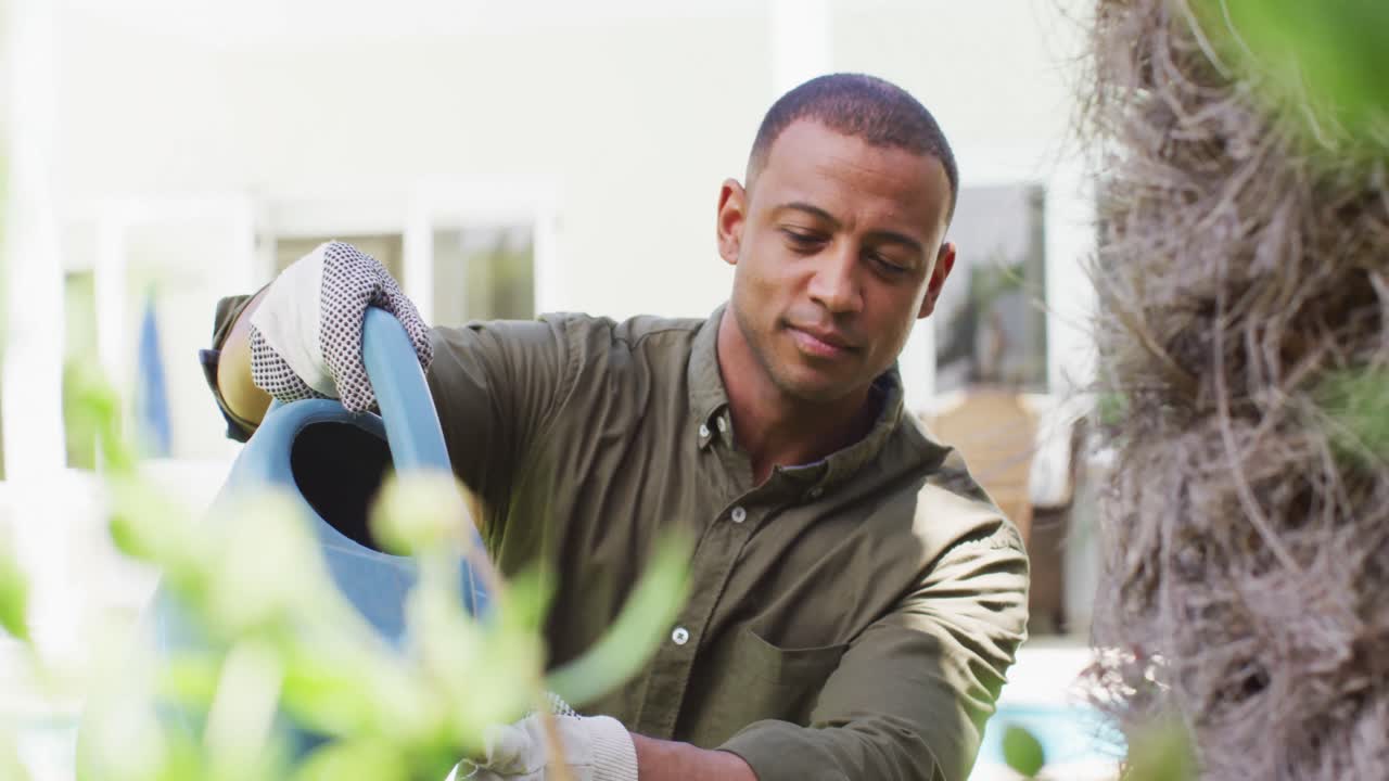 Portrait of biracial man gardening, watering plants with watering can