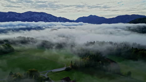 eine umgekehrte luftaufnahme eines kleinen dorfes in einer mit nebel bedeckten rustikalen landschaft in österreich