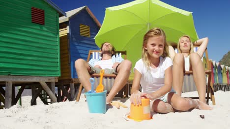 Girl-playing-with-sand-while-family-relaxing-at-beach