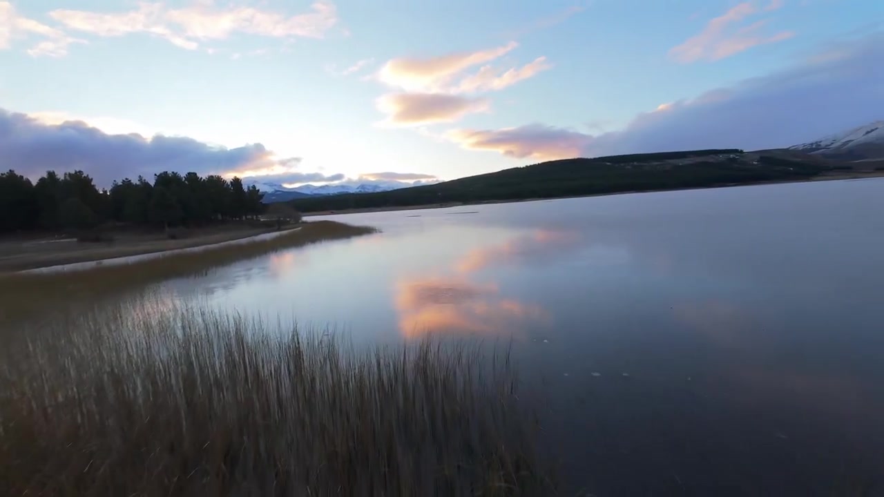 Esquel, Chubut, Arjantin yakınlarındaki Laguna La Zeta, göl kenarı pavyonu, ahşap iskeleler, sazlık sulak alanlar ve akşam gökyüzü altında Patagonya orman manzarası ile FPV yörünge ve ileri uçuş çekimi.