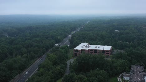 imágenes aéreas que muestran una carretera suburbana pasando por un solitario edificio de oficinas hacia colinas cubiertas de árboles en la niebla.