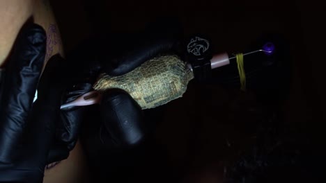 Close-up-slow-motion-vertical-handheld-shot-of-a-tattoo-artist-tattooing-a-client-and-adding-shading-with-the-needle-penetrating-the-skin-in-a-dark-studio-room