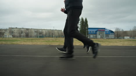 side view of an adult and two young boys jogging together with the same pace on a stadium track, with buildings visible in the background