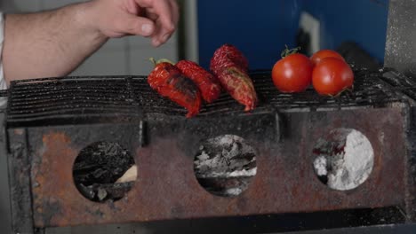 cook puts tomatoes and peppers on charcoal fire grill to prepare healthy mediterranean cuisine