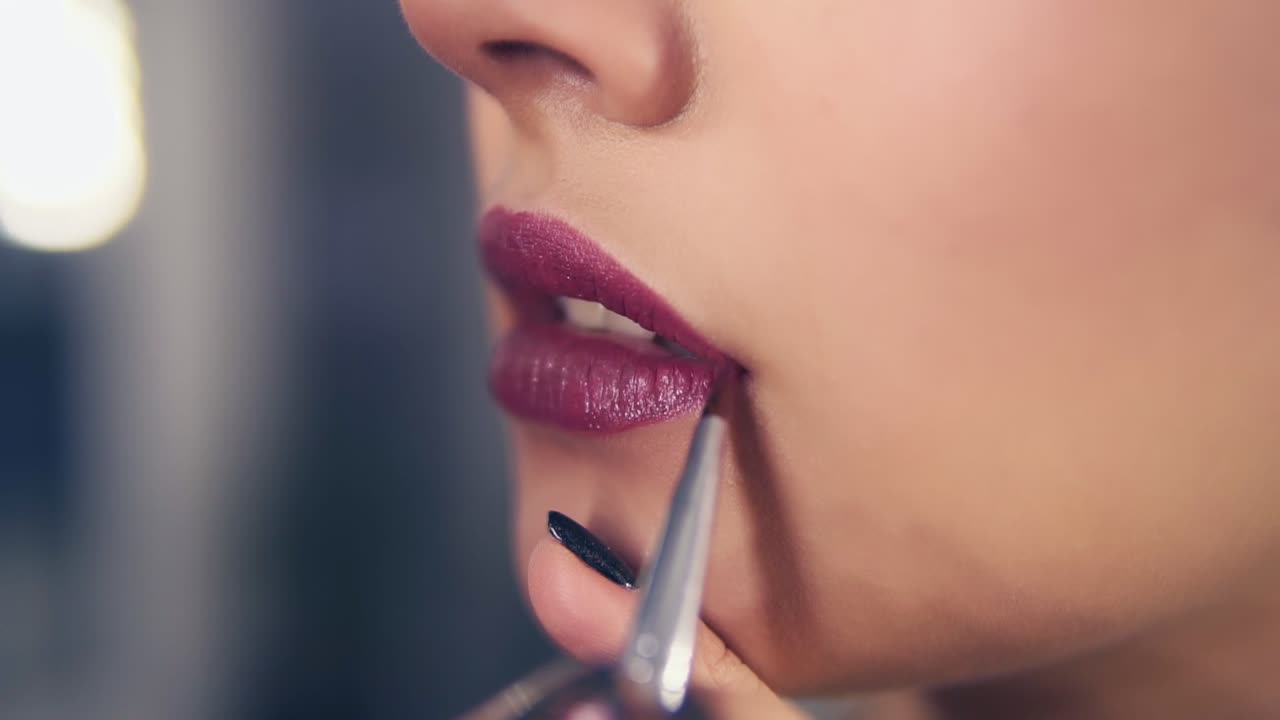 Unrecognizable professional makeup artist using special brush to apply lipstick on model's lips working in beauty fashion
