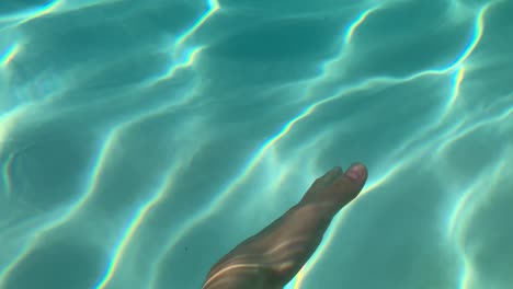 une main joue avec la texture de la lumière se reflétant sur l'eau, dans la piscine