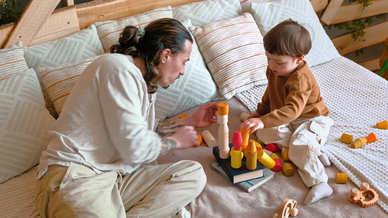 Man playing with child with colourful wooden toys on the bed